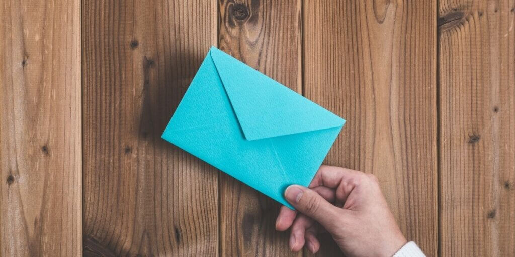 Hand holding blue nevelope in front of wood paneling